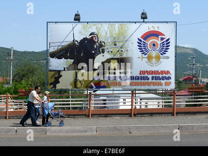 Stepanakert, Repubblica di Nagorno-Karabakh. Il 25 giugno, 2014. Pedoni passare un poster di propaganda che mostra un salutando i soldati a un serbatoio nel centro di Stepanakert, Repubblica di Nagorno-Karabakh, 25 giugno 2014. La Repubblica di Nagorno-Karabakh è indipendente de facto ma lo stato non riconosciuto disputata tra Armenia e Azerbaigian. La regione senza sbocchi sul mare nel Caucaso del Sud è abitata da armeni. Foto: Jens Kalaene - NESSUN SERVIZIO DI FILO-/dpa/Alamy Live News Foto Stock