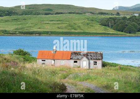 Abbandonate case crofters da un loch in campagna sull'Isola di Skye in Scozia UK uno con un rosso tetto dello stagno. Foto Stock