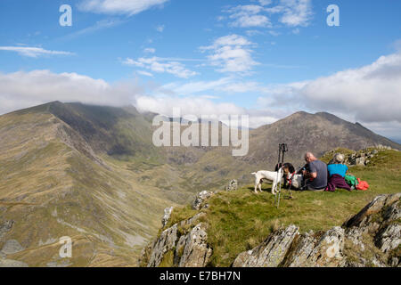 Gli escursionisti che riposano sulla cima Yr Aran con vista attraverso CWM Llan fino alla vetta nuvolosa Snowdon sulle montagne del Parco Nazionale Snowdonia Galles del Nord Regno Unito Foto Stock