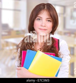 Ritratto di Cute girl teen in piedi in aula con libri colorati in mani, la preparazione alla lezione, si torna a scuola Foto Stock