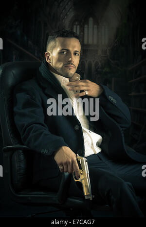 Elegante uomo seduto in una sedia tenendo la pistola su sfondo scuro Foto Stock