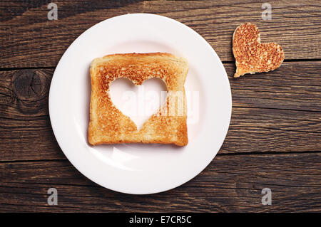 Fetta di pane tostato con taglio fuori forma di cuore su sfondo di legno Foto Stock