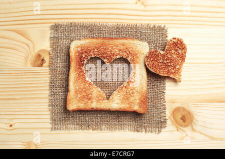 Fetta di pane tostato con taglio fuori forma di cuore sul tavolo di legno Foto Stock