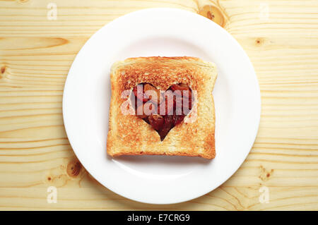 Fetta di pane con taglio in forma di cuore e uva passa su un tavolo di legno Foto Stock