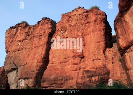 Enorme roccia verticale superfici imbevuto di colore giallo rossiccio luce del sole di mattina a Badami, Karnataka, India, Asia Foto Stock