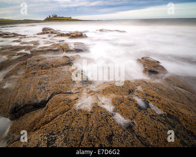 Incredibilmente aspra costa di Isola Santa in Northumberland è protetto dal castello di Dunstanburgh Foto Stock