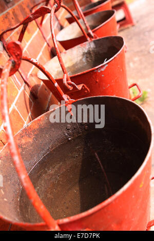 Benne di fuoco in vecchio stile acqua secchielli riempiti e pronto per l'uso appeso a una parete esterna Foto Stock