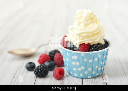 Le fragole fresche con panna montata nel bicchiere di carta su sfondo di legno Foto Stock