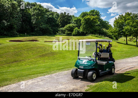 Bunker da un putting green con flagstick e foro e un buggy elettrico o il carrello su un tipico campo da golf. Foto Stock