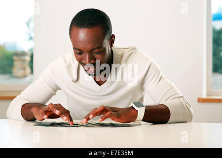 Ritratto di un felice african uomo seduto sul tavolo con banconote di dollari USA Foto Stock