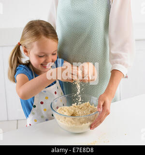 Ragazza strofinando la farina e il burro insieme per far sì che la pasta biscotto, 5 anni Foto Stock