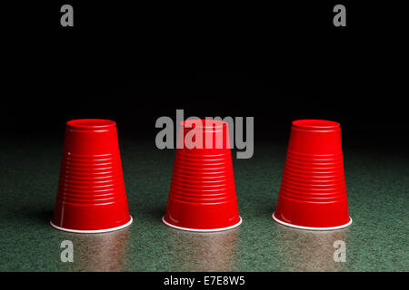 Gioco di Shell - tre tazze di colore rosso su un tavolo verde disposto come il gioco della shell. Copia dello spazio. Foto Stock