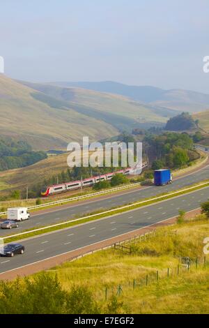 Classe 390 Pendolino Virgin treno passa l autostrada M6 nel fiume Lune Valley. Howgills, Cumbria, Linea principale della costa occidentale, UK. Foto Stock