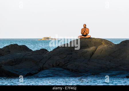 Un uomo è in meditazione, la pratica dello yoga su una roccia, Kudle Beach, Gokarna, Karnataka, India Foto Stock
