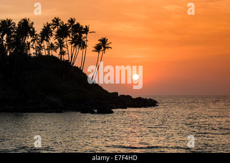 Tramonto sulla spiaggia con rocce e alberi di palma, Palolem Beach, Canacona, Goa, India Foto Stock