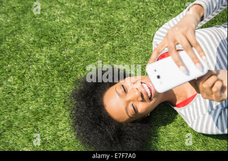 African American donna posa in erba tramite telefono cellulare Foto Stock