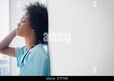 African American nurse appoggiata contro la parete Foto Stock