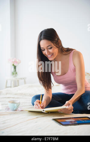 Donna prendendo appunti con computer tablet sul letto Foto Stock