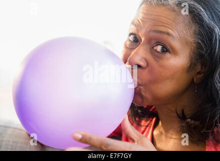 Razza mista donna palloncino soffia sul divano Foto Stock