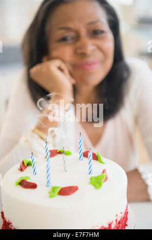 Razza mista donna che spegne le candeline sulla torta del compleanno sulla torta Foto Stock