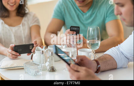 Amici ispanica utilizzando i telefoni cellulari in cafe Foto Stock