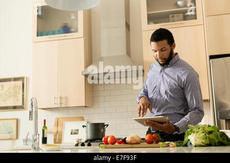 Razza mista uomo cucinare con il tablet pc in cucina Foto Stock