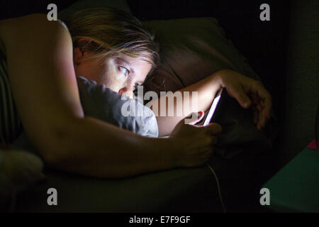 La donna caucasica tramite telefono cellulare a letto Foto Stock