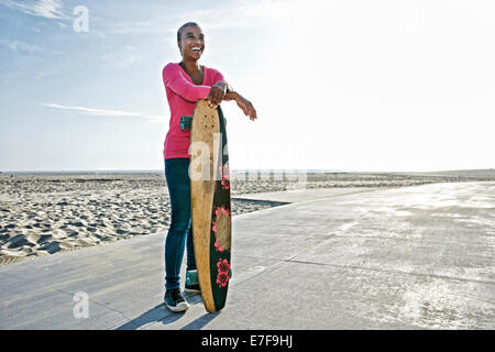 I vecchi Nero donna azienda skateboard sulla spiaggia Foto Stock