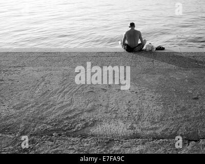 Muscoloso uomo seduto al dock, guardando il mare. Fotografato a Vrsar, Croazia. Foto Stock