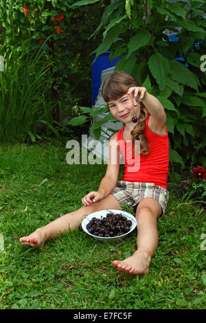 Carino bambina di mangiare le ciliegie in giardino Foto Stock