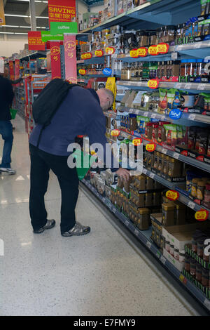 Un uomo selezionando 'propria marca' di caffè in un Asda store. Foto Stock