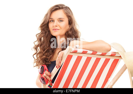 Bella donna seduta sulla sedia a sdraio e occhiali da sole di contenimento isolato su sfondo bianco Foto Stock