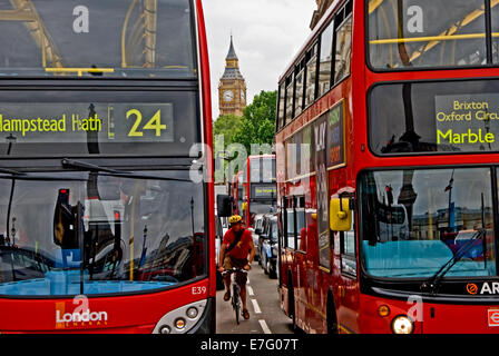 Un ciclista stringe attraverso uno spazio tra due autobus rossi di Londra mentre in attesa ad un semaforo. Foto Stock