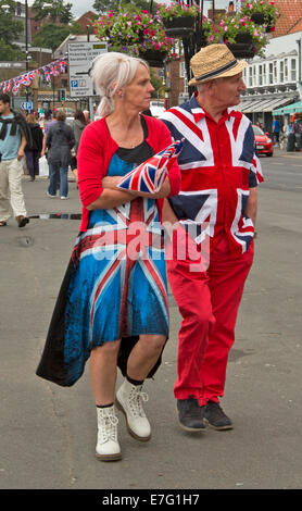 Coppia di anziani vestiti in luminose e inusuali abiti realizzati dalla Union Jack bandiera britannica e portante bandiera a Whitby Inghilterra Foto Stock