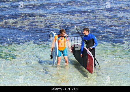 Due giovani uomini in piedi in acqua a parlare dopo una sessione di surf e stand up paddleboarding (SUP) in Western Australia. Foto Stock