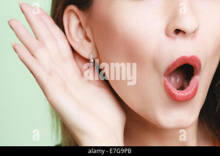 Closeup emotiva di scioccato donna sorpreso la ragazza con la mano per orecchio segreto di ascolto gossip o suono tranquillo sul verde. Foto Stock