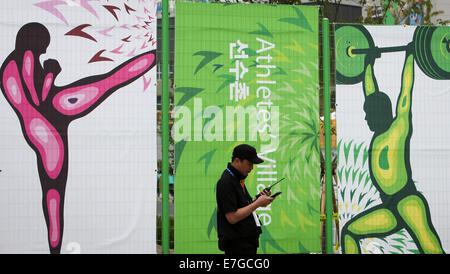 (140917) -- INCHEON, Sett. 17, 2014 (Xinhua) -- una guardia di sicurezza si trova di fronte dei manifesti nel Villaggio Atleti in Incheon, Corea del Sud, Sett. 17, 2014. Il Villaggio Atleti è situato a dieci chilometri di distanza dalla principale premere Centro. Esso consiste di 22 edifici di appartamenti, che forniscono un totale di 2.200 camere. Xvii giochi asiatici che si terrà dal 7 settembre 19 ott. 4. (Xinhua/Zhang Fan)(Lz) Foto Stock