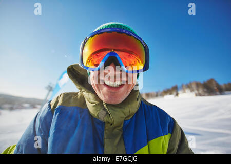 Sorridente snowboarder guardando la telecamera attraverso occhiali protettivi a winter resort Foto Stock