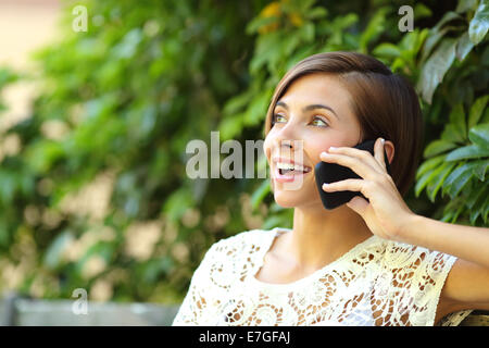 Casual donna felice sul telefono in un parco seduta su una panchina con un Verde come sfondo sfocato Foto Stock