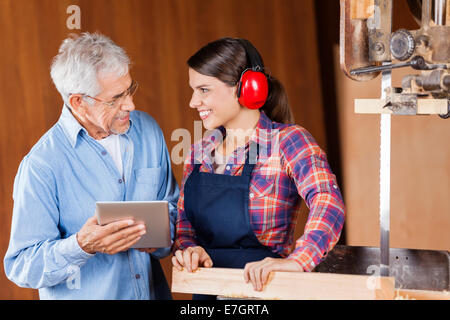 Carpenter con tavoletta digitale mentre guarda il collega Foto Stock