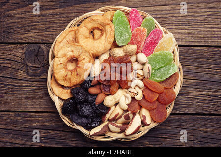 Frutta secca e noci in una ciotola di vimini su vintage sfondo di legno Foto Stock