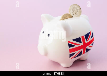 Salvadanaio con britannica Union Jack e due sterling pound monete nella slot su un sfondo di colore rosa. Regno Unito, Gran Bretagna Foto Stock