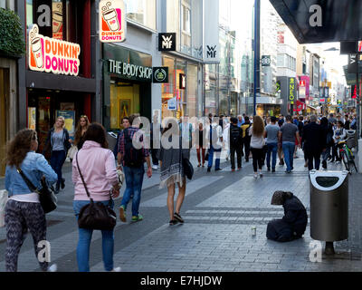 Trafficata strada principale dello shopping di Colonia, in Germania con molti peoplepassing e la donna per l'accattonaggio denaro Foto Stock