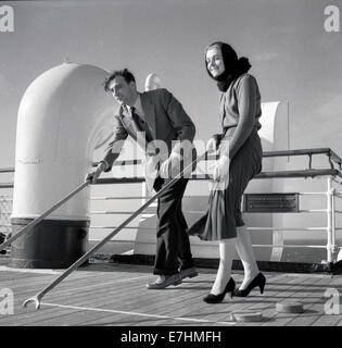 1950s. Un quadro storico di due ben vestito di passeggeri su una nave da crociera godendo un deck porta gioco di spingere il puck. Foto Stock