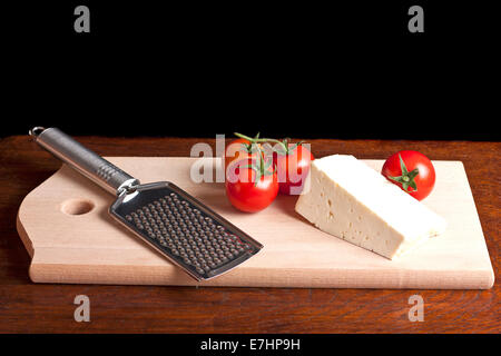 Formaggio, grattugia e rosso pomodoro su una scrivania in legno Foto Stock