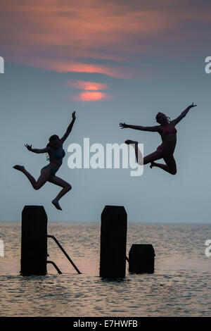 Aberystwyth, Wales, Regno Unito. 18 Settembre, 2014. Aberystwyth Wales UK, giovedì 18 settembre 2014 come il sole tramonta oltre la calma piatta acque di Cardigan Bay, due ragazze godere il caldo settembre estate indiana, immersioni subacquee e salta fuori il pontile a Aberystwyth sulla West Wales coast. L'incantesimo di liquidare ed insolitamente caldo è previsto per estendersi nel corso del prossimo weekend, ma con il rischio di thundery condizioni e alcune heavy rain foto ©Keith Morris / Alamy Live News Foto Stock