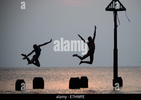 Aberystwyth, Wales, Regno Unito. 18 Settembre, 2014. Come il sole tramonta oltre la calma piatta acque di Cardigan Bay, due ragazze godere il caldo settembre estate indiana, immersioni subacquee e salta fuori il pontile a Aberystwyth sulla West Wales coast. L'incantesimo di liquidare ed insolitamente caldo è previsto per estendersi nel corso del prossimo weekend, ma con il rischio di thundery condizioni e alcune heavy rain Photo credit: Keith Morris/Alamy Live News Foto Stock