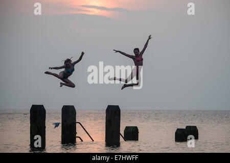 Aberystwyth, Wales, Regno Unito. 18 Settembre, 2014. Come il sole tramonta oltre la calma piatta acque di Cardigan Bay, due ragazze godere il caldo settembre estate indiana, immersioni subacquee e salta fuori il pontile a Aberystwyth sulla West Wales coast. L'incantesimo di liquidare ed insolitamente caldo è previsto per estendersi nel corso del prossimo weekend, ma con il rischio di thundery condizioni e alcune heavy rain Photo credit: Keith Morris/Alamy Live News Foto Stock