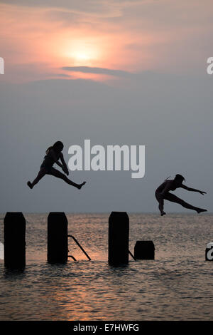 Aberystwyth, Wales, Regno Unito. 18 Settembre, 2014. Come il sole tramonta oltre la calma piatta acque di Cardigan Bay, due ragazze godere il caldo settembre estate indiana, immersioni subacquee e salta fuori il pontile a Aberystwyth sulla West Wales coast. L'incantesimo di liquidare ed insolitamente caldo è previsto per estendersi nel corso del prossimo weekend, ma con il rischio di thundery condizioni e alcune heavy rain Photo credit: Keith Morris/Alamy Live News Foto Stock