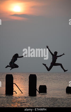 Aberystwyth, Wales, Regno Unito. 18 Settembre, 2014. Come il sole tramonta oltre la calma piatta acque di Cardigan Bay, due ragazze godere il caldo settembre estate indiana, immersioni subacquee e salta fuori il pontile a Aberystwyth sulla West Wales coast. L'incantesimo di liquidare ed insolitamente caldo è previsto per estendersi nel corso del prossimo weekend, ma con il rischio di thundery condizioni e alcune heavy rain Photo credit: Keith Morris/Alamy Live News Foto Stock